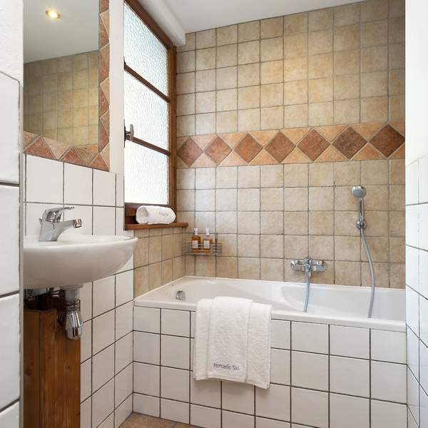 Two bathrooms have a bath with hand held shower, sink and toilet